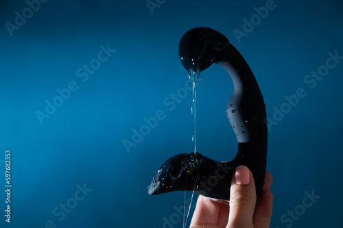 A woman pours lubricant on a black prostate stimulator on a blue background. Men's health prevention concept.