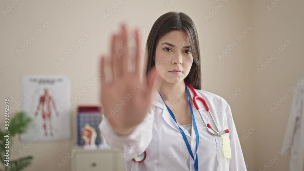Young beautiful hispanic woman doctor doing stop gesture with hand at clinic Young beautiful hispanic woman doctor doing stop gesture with hand at clinic