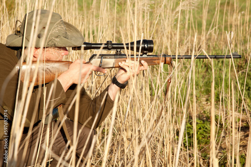 Nature, wildlife and male hunter with a shotgun while in camouflage shooting in outdoor field. Grass, safari and man hunting animals with rifle weapon hiding in plants to shoot target in countryside.