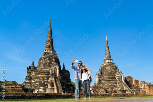young foreign couple tourist taking selfie photo or making video call at Wat Phra Si Sanphet in Ayutthaya historical park, UNESCO attractive pagoda ancient temple while traveling on holiday vacation