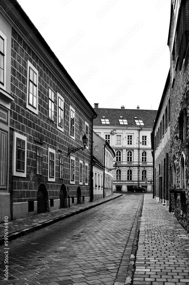 Narrow alley in old part of downtown Budapest. black and white photo. stucco exterior facades and framed wood windows. cobblestone pavement. vintage style exterior wall facades. old street.