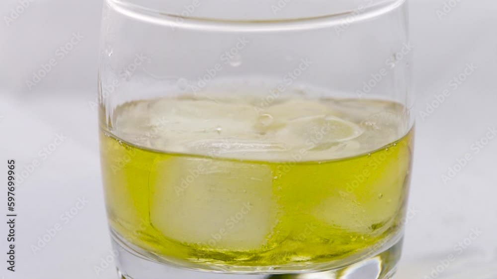 Glass of whiskey with ice cube. Alcohol pouring in the glass from the bottle. Scotch on the rocks. Slider shot. Dark, rustic, background. Glass of whiskey with ice cube. Alcohol pouring in the glass from the bottle. Scotch on the rocks. Slider shot. Dark, rustic, background.