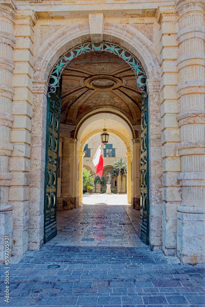 Arch at entrance of Grandmaster's Palace with with maltesian flag in the background r on a sunny hot summer day. Photo taken August 9th, 2017, Valletta, Malta.