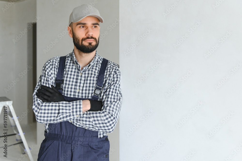 Portrait of handsome mechanic with stubble in blue overall, shirt having his arms crossed, looking at camera