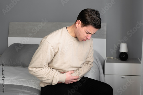 Young man with stomach ache sitting on the bed in his room