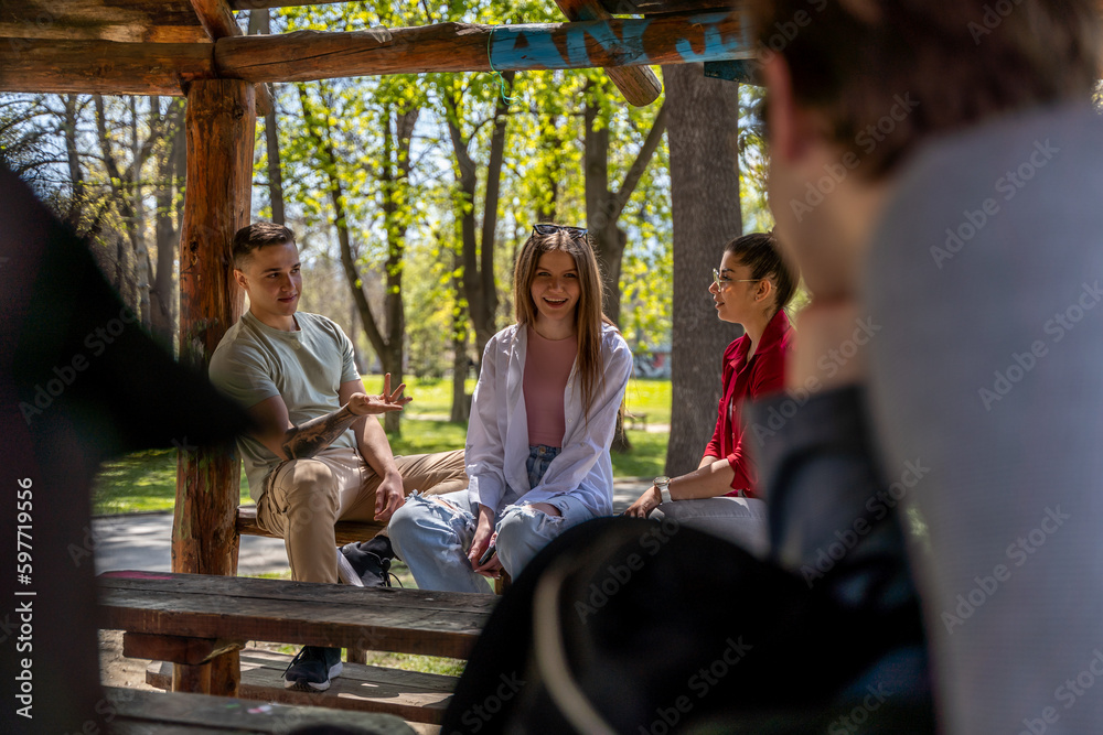 Obraz premium Happy young people sitting on wooden bench in the park