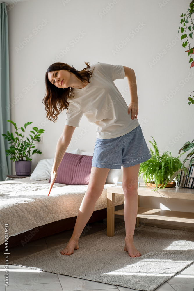 Energetic fit woman keeping body in good shape, doing exercises at home, makes bends. Self care and positive emotions.