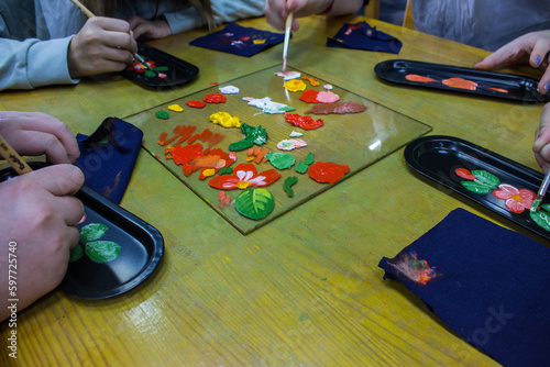Zhostovo, Moscow region, Russia - October, 14, 2022: master class - painting a small black tray with bright flowers and leaves while holding brushes and paints at the table and copy space