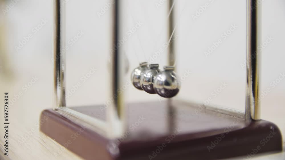 Metal balls of Newton cradle swing hanging on rack closeup. Balancing device for mindfulness improvement on office table Metal balls of Newton cradle swing hanging on rack closeup. Balancing device for mindfulness improvement on office table