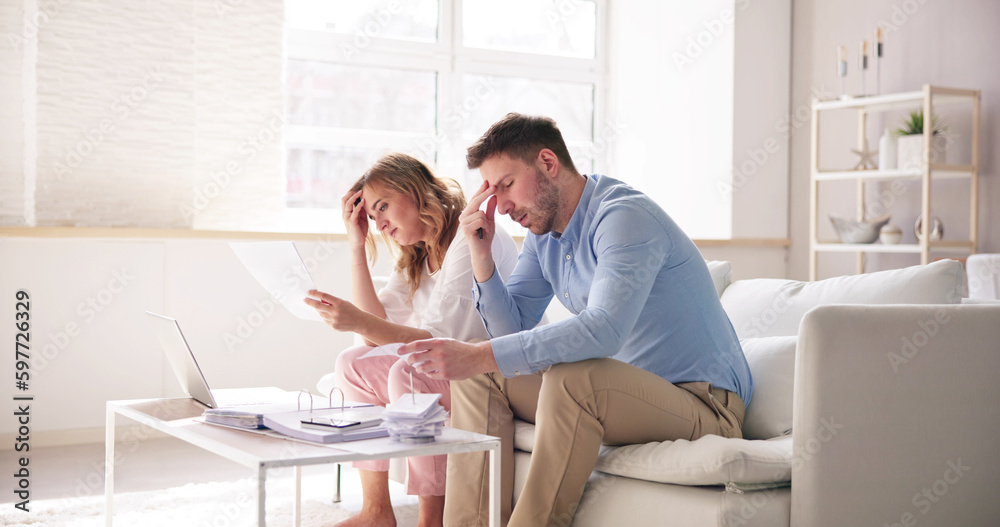Shocked Young Couple Sitting On Sofa Looking At Bill Shocked Young Couple Sitting On Sofa Looking At Bill
