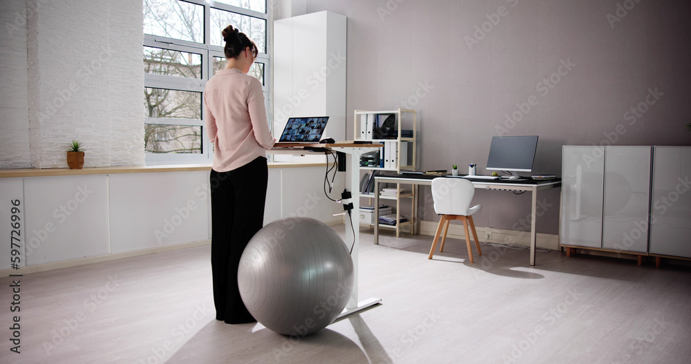 Fototapeta premium Woman Using Adjustable Height Standing Desk In Office
