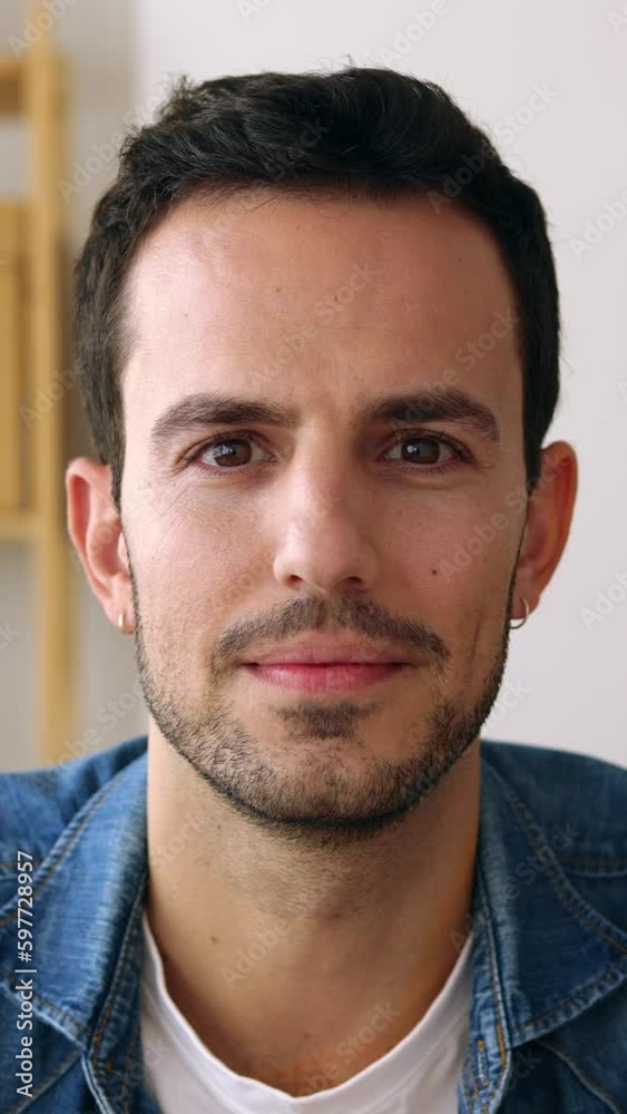 POV camera view or vertical screen mobile phone front portrait of happy good-looking millennial guy sitting on table at home. Smiling headshot of young adult man smiling at camera from home office.