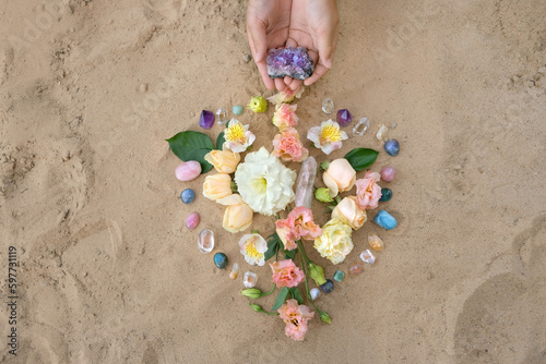 Hands with gemstones and flowers for Crystal Ritual on sand natural background. Esoteric spiritual wiccan practice for relax, harmony, life balance. spa concept. Flower Mandala with crystals. top view photo