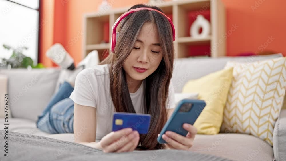 Young chinese woman shopping with smartphone and credit card listening to music at home Young chinese woman shopping with smartphone and credit card listening to music at home