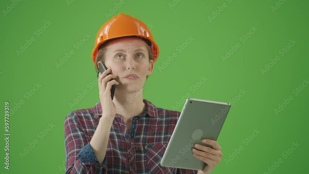 Green Screen.Young Confident Female Civil Engineer in Checkered Shirt and Hard Hat Emotionally Talking with Colleague on Phone and Looking to the Tablet.Women at Work Concept. Team Work Concept. Green Screen.Young Confident Female Civil Engineer in Checkered Shirt and Hard Hat Emotionally Talking with Colleague on Phone and Looking to the Tablet.Women at Work Concept. Team Work Concept.