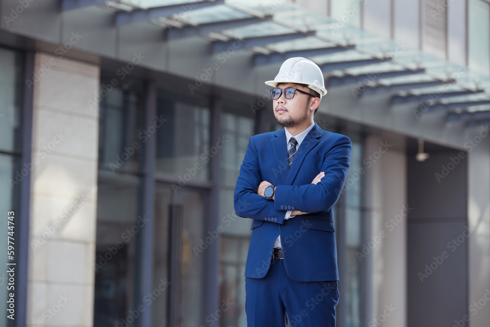 Handsome engineer wearing suit and hard hat or white helmet on building background. Engineer using tablet for checking construction about modern building. copy space for text. Handsome engineer wearing suit and hard hat or white helmet on building background. Engineer using tablet for checking construction about modern building. copy space for text.