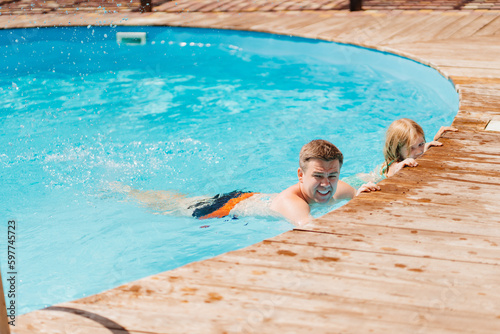 Dad and daughter have fun and swim at the edge of the pool 