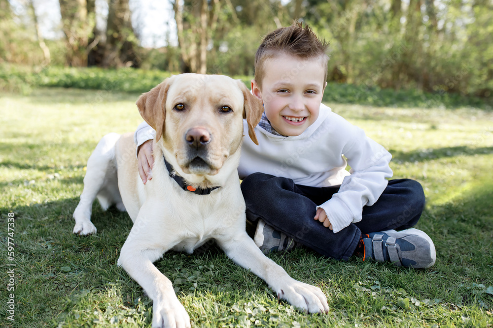 Love and pets. Positive happy boy hugs his pet, rests with a labrador on the grass. soft focus on dog Love and pets. Positive happy boy hugs his pet, rests with a labrador on the grass. soft focus on dog
