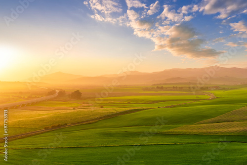 scenery rural view of a contryside farm in green fields and hills with amazing cloudy sky on background