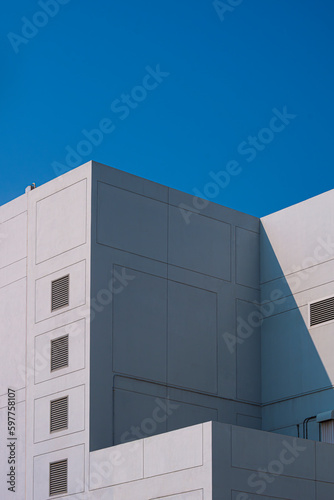 Low angle view of white modern geometric building with air vent on concrete wall surface against blue clear sky in vertical frame  Street Architecture Background concept