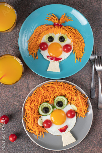 Fun Food for kids - smiling faces boy and girl made from fried eggs, carrot, cucumbers, crerry tomato, black olives on plates. Creative healthy breakfast for children photo