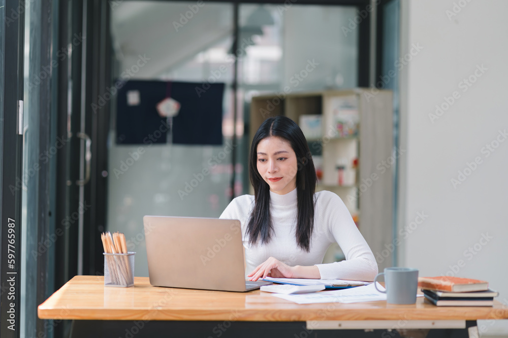 Portrait of a successful and lovely millennial Asian businesswoman, secretary, sales manager, or business consultant, sitting at her workplace with a laptop, smiling, while dressed casually. Portrait of a successful and lovely millennial Asian businesswoman, secretary, sales manager, or business consultant, sitting at her workplace with a laptop, smiling, while dressed casually.