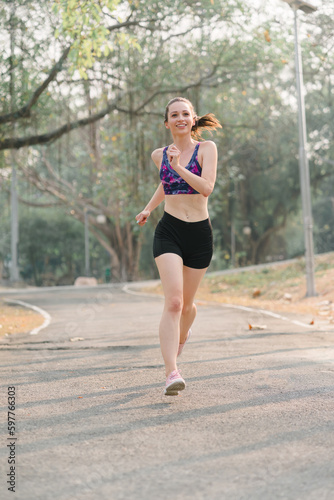 A beautiful sportswoman in sportswear is jogging outdoors in Autumn city park background.