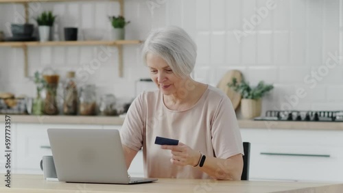 beautiful elderly woman pensioner doing online shopping with bank card and laptop at home with laptop
