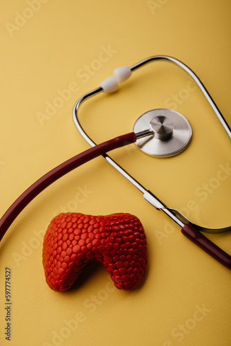 Stethoscope and red model of thyroid gland on a yellow background. Vertical image