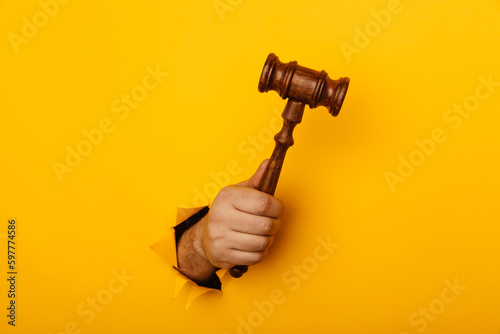Hand holding a judge's gavel through torn yellow background. Law concept
