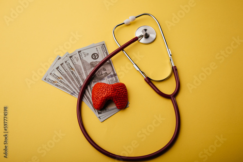 Model of thyroid gland, dollar banknotes and stethoscope on a yellow background. Health care insurance or savings