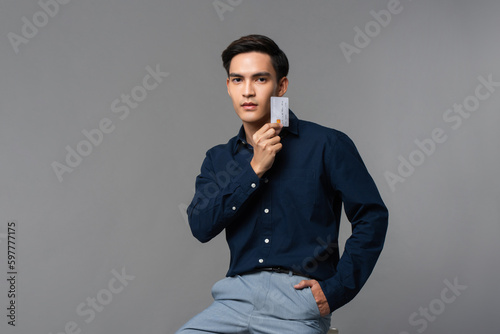 Handsome Asian man showing credit card in light gray isolated background studio shot