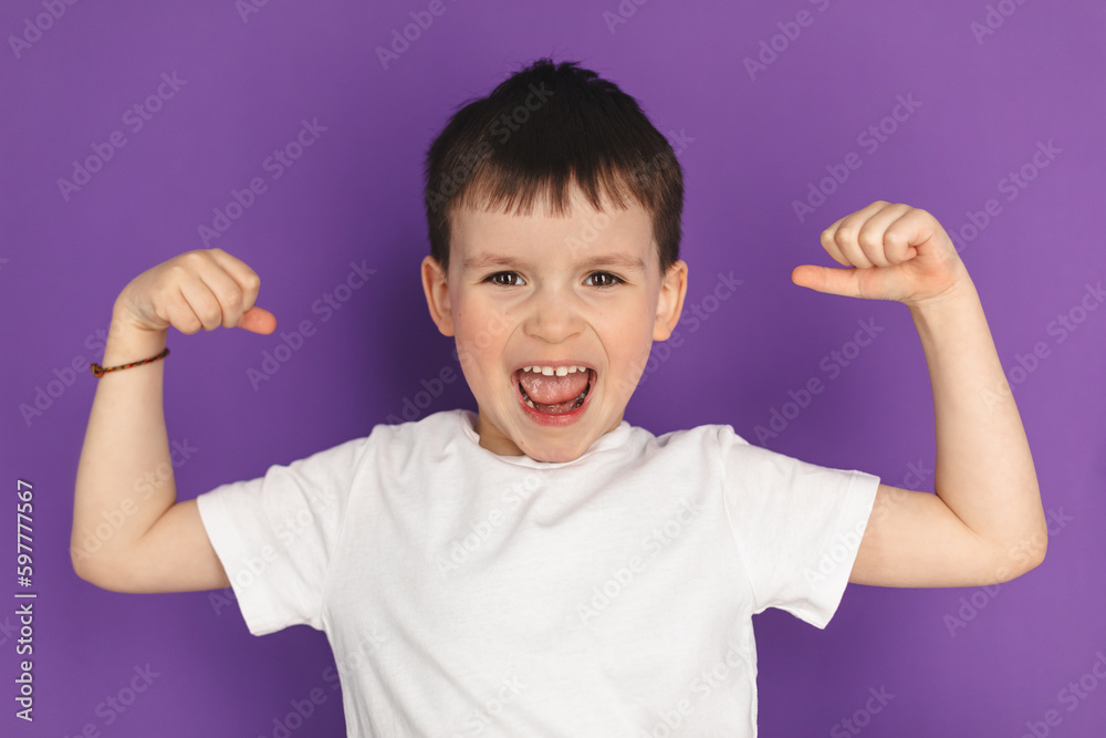 Little brunette boy in white t-shirt show strong arm gesture, powerful isolated purple background. Funny little power super hero kid showing muscles. Strength, confidence or defense from bullying. Little brunette boy in white t-shirt show strong arm gesture, powerful isolated purple background. Funny little power super hero kid showing muscles. Strength, confidence or defense from bullying.