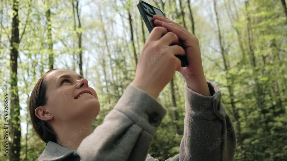 Happy young brunette woman using smartphone in spring forest. Traveler female hiker using phone. Cute girl hiker takes smart phone pic of beautiful woods. Concept adventure travel blogger wanderlust Happy young brunette woman using smartphone in spring forest. Traveler female hiker using phone. Cute girl hiker takes smart phone pic of beautiful woods. Concept adventure travel blogger wanderlust