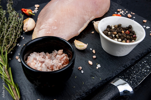 Spices and raw chicken breast on black, diet raw meat