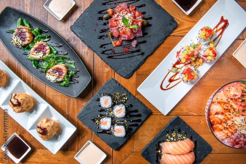 Fototapeta Naklejka Na Ścianę i Meble -  Symmetrical composition of Japanese food from above on wooden table, sushi, sashimi, tempura, salmon poke , fish bawls, tuna tartare and vegetables. 