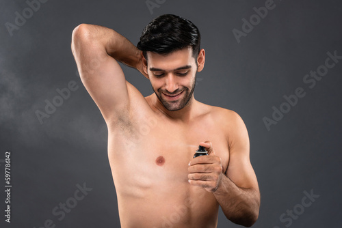 Shirtless handsome Caucasian man using deodorant body spray in light gray isolated background studio shot