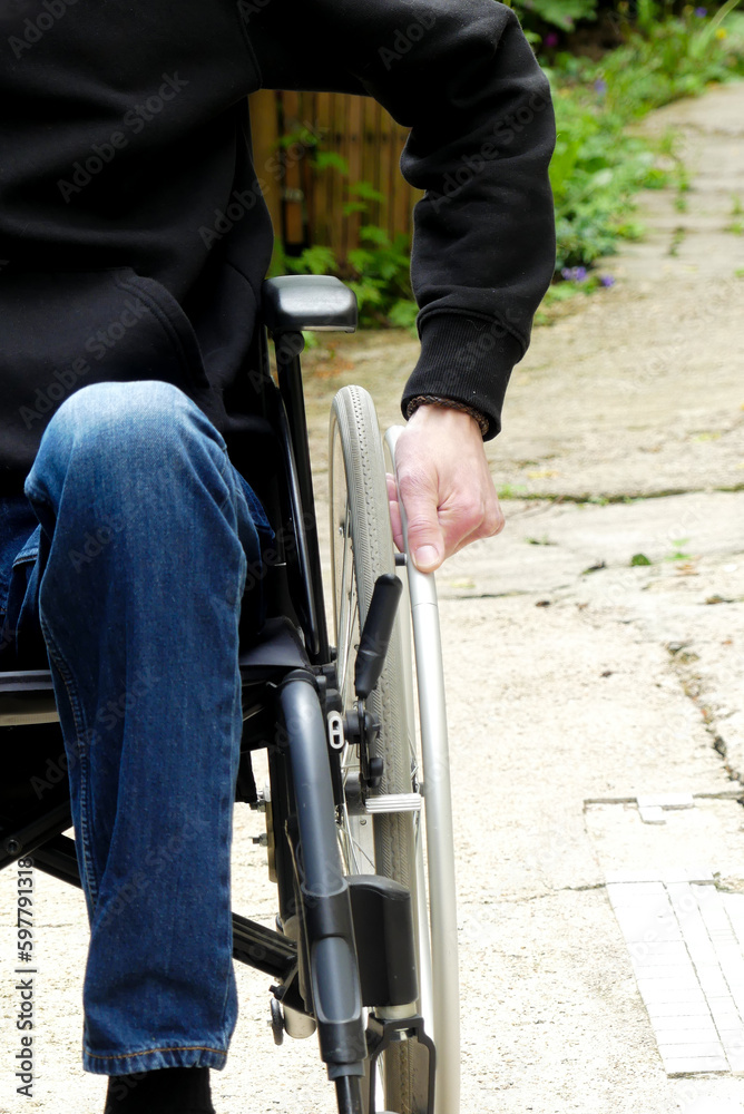 A disabled person in a wheelchair. A man with reduced mobility in an alley with vegetation.