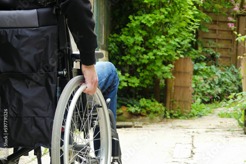 A disabled person in a wheelchair. A man with reduced mobility in an alley with vegetation.