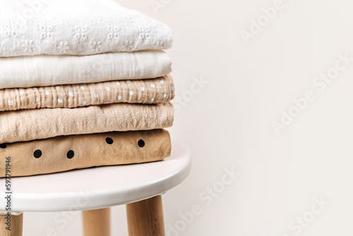Stack of baby clothes. Cotton clothes and muslin swaddle blanket in white and beige colors. Clean freshly laundered, neatly folded kids clothes on table. photo