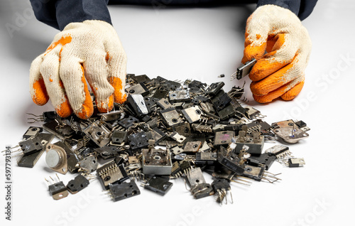 Close up of man hands wearing gloves with ICs, transistors, diodes isolated on white background. Stacks of used electronic components, e-waste photo