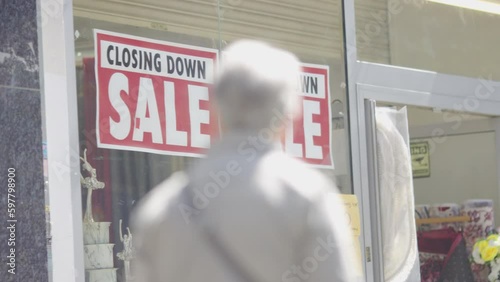 Closing down sale sign on a high street shop as pedestrians walk past, in slow motion