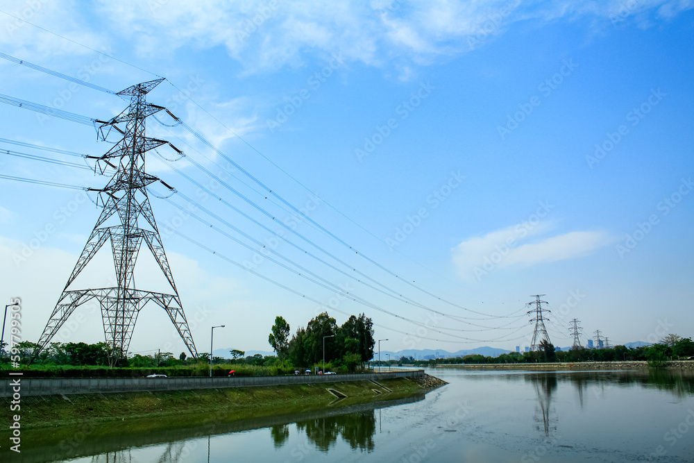 A High voltage post, and electrical transmission tower with high voltage lines under the blue sky background. High voltage tower against the road and river in countryside.