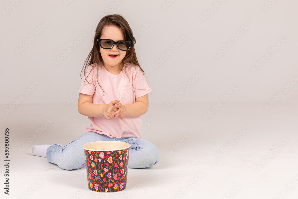 Cheerful little girl in 3D glasses preparing to watch the film while holding popcorn over white background. Cinema and movie concept Cheerful little girl in 3D glasses preparing to watch the film while holding popcorn over white background. Cinema and movie concept