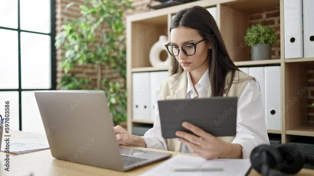 Young beautiful hispanic woman business worker using touchpad and laptop at office