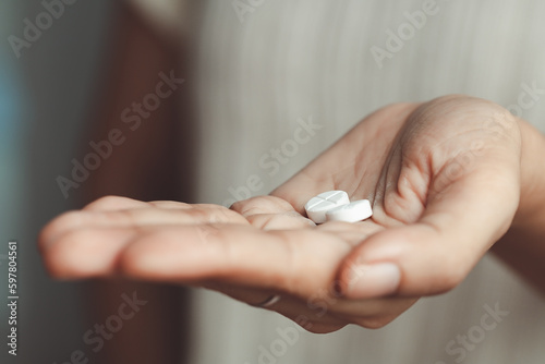 Two white pills on asian woman's hand for medical and healthcare concept.