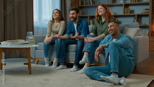 Four diverse ethnicity friends watch television at home cinema people spectators watching smart tv channel comedy show serial movie multiracial african american caucasian women men laughing enjoy film