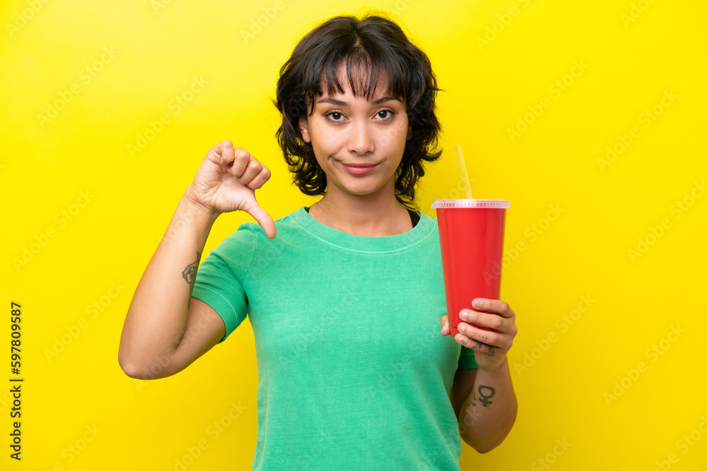 Young Argentinian woman holding a soda isolated on yellow background showing thumb down with negative expression Young Argentinian woman holding a soda isolated on yellow background showing thumb down with negative expression
