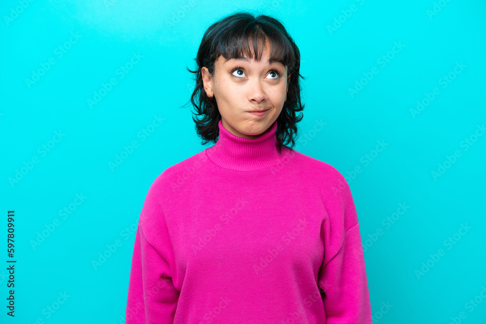 Young Argentinian woman isolated on blue background and looking up Young Argentinian woman isolated on blue background and looking up
