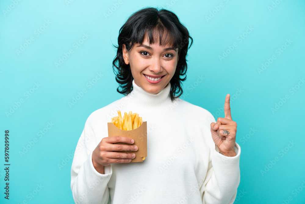 Young Argentinian woman holding fried chips isolated on blue background pointing up a great idea Young Argentinian woman holding fried chips isolated on blue background pointing up a great idea